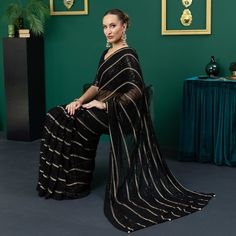 Introducing the bewitching Damia, a saree so enchanting, it will leave you spellbound. In shimmering black chiffon, this pre-pleated saree is adorned with intricate threadwork and twinkling sequins that shimmer with every step you take. Dazzling from every angle, the short net blouse glitters with an array of sequins, while the deep back of the blouse features sultry tassels that add a touch of allure to the look. The 3/4 semi-sheer sleeves add a hint of subtle grace to this striking ensemble. The black silk petticoat provides an ideal canvas for the saree, allowing its bewitching beauty to truly stand out. Indulge in the magic of Damia and captivate all those around you. Saree:  Color: Black  Fabric: Chiffon Preplated sari with sequins and threadwork all over  Short net blouse with sequin Elegant Evening Saree For Festivals, Elegant Party Saree In Georgette, Elegant Party Georgette Saree, Traditional Chiffon Pre-draped Saree For Party, Chiffon Pre-draped Saree For Eid Party, Georgette Evening Saree For Festivals, Georgette Saree For Evening Festivals, Elegant Georgette Pre-draped Saree For Celebrations, Elegant Chiffon Pre-draped Saree For Festivals