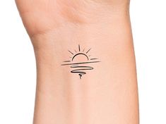 a small sun tattoo on the wrist is shown in black ink, and it appears to be drawn by hand