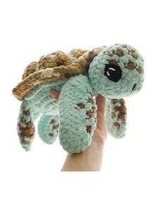 a crocheted turtle is held up in the air by someone's hand