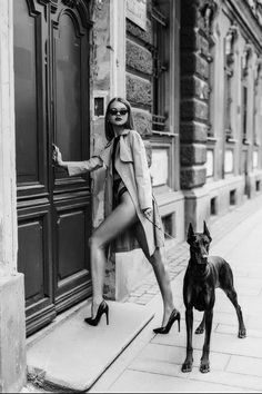 a woman in high heels standing next to a dog on the sidewalk with her leg up