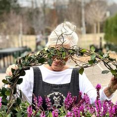 an older woman is standing in the middle of purple flowers with her hands over her head