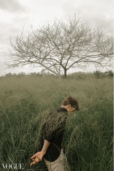 a man is walking through tall grass in front of a tree