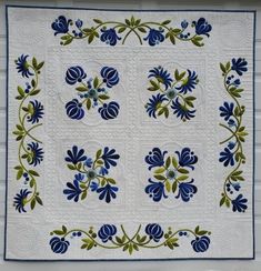 a blue and green quilt hanging on the side of a white building with flowers in it