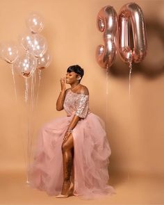 a woman in a pink dress sitting next to balloons