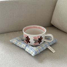 a coffee cup sitting on top of a blue and white checkered pillow next to a tag