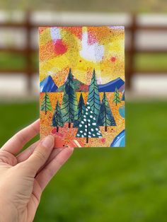 a hand holding up a small card with trees on it