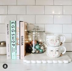 two mugs sitting on top of a counter next to books