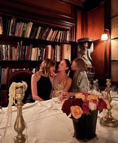 three women sitting at a table in front of bookshelves with wine glasses on it