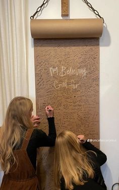 two women writing on a cork board with chains hanging from the top and below them