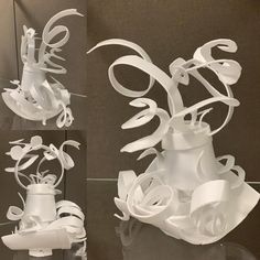 three white sculptures made out of paper on a glass table with black wall behind them