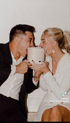 a man and woman sitting next to each other holding a cake in front of their face