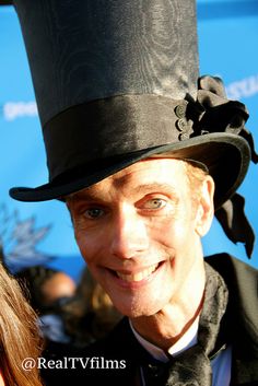 a man wearing a top hat and bow tie at an outdoor event smiling for the camera