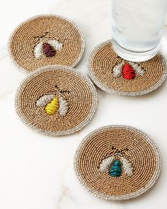 four coasters with beaded bees on them next to a water glass and spoon