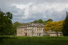 an old house with trees in the foreground and clouds in the sky above it