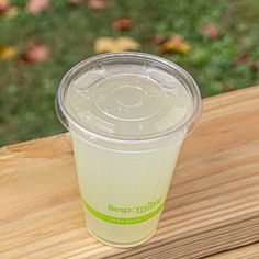 a plastic cup sitting on top of a wooden table next to a green grass covered field