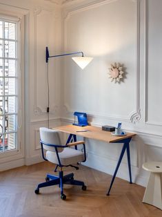 an office with a desk, chair and lamp on the wall in front of a window