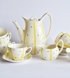 a white tea set with yellow and blue designs on the front, sitting next to other cups and saucers