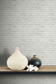 two vases sitting on a shelf in front of a brick wall with white flowers