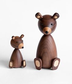 a wooden bear and cub sitting next to each other on a white surface with one brown bear looking at the camera