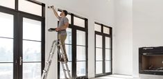 a man standing on a ladder in front of a fire place and painting the wall