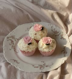 three cupcakes with white frosting and pink flowers are on a floral plate