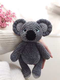 a hand holding a gray knitted teddy bear