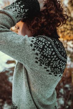 a woman with curly hair wearing a gray sweater and black pants standing in the snow