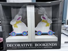 two decorative bookends in the shape of rabbits with yellow and blue bows on their heads