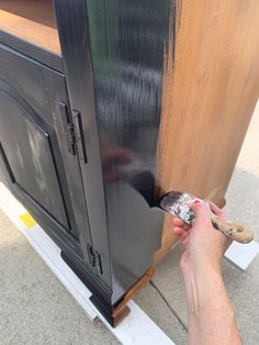 a person is painting the side of a wooden cabinet with black paint on it's sides