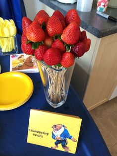 strawberries are arranged in a vase on a blue table cloth with a yellow plate next to it