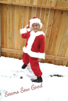 a young boy dressed in santa claus costume standing in the snow with his hand on his head