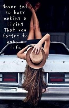 a woman laying on the hood of a car with her legs up and hat over her head