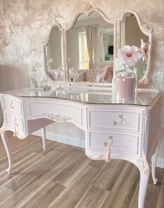 a white dressing table with a mirror and vase on it in a room that has pink wallpaper