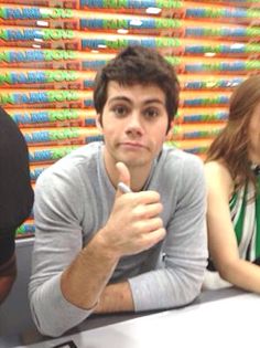 two people sitting at a table in front of stacks of books with one pointing to the camera