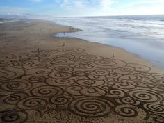 an intricately designed sand art on the beach with people walking in the water behind it