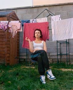 a woman sitting on a chair in front of clothes hanging out to dry her clothes