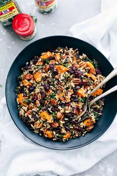 a bowl filled with rice and vegetables on top of a white cloth next to two spoons