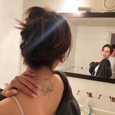 a woman with her back turned to the camera in front of a bathroom mirror, and another person taking a selfie