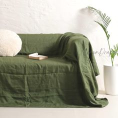 a green couch with a book on it and a plant in the corner next to it