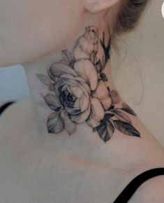 a woman's neck with a flower tattoo on her left shoulder and behind the neck is a white rose