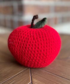 a crocheted red apple sitting on top of a wooden table