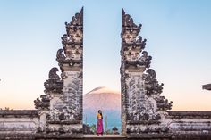 a woman standing in front of an ornate gate with mountains in the background at sunset