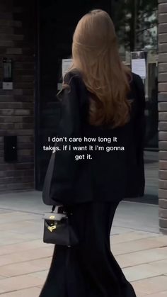 a woman walking down the street with her back turned to the camera, wearing a long black dress and carrying a handbag