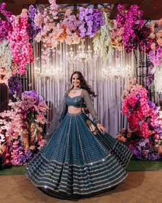 a woman in a blue and gold lehenga with flowers on the wall behind her