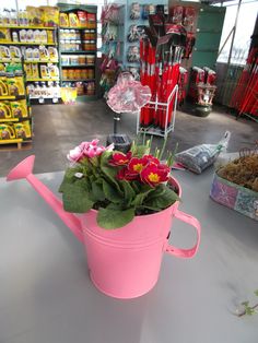 a pink watering can filled with flowers sitting on top of a table in a store