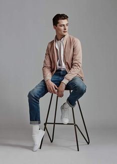 a young man sitting on top of a stool wearing jeans and a pink cardigan