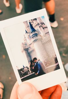 a person holding up a polaroid with a castle in the background