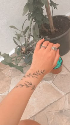 a woman's hand with a ring on her left wrist next to a potted plant