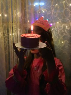 a girl holding up a birthday cake in front of her face with a lit candle on it