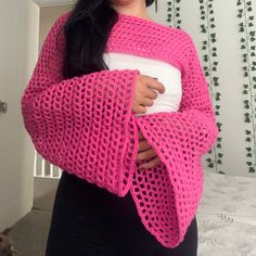 a woman is wearing a pink crocheted shawl and holding a white pillow